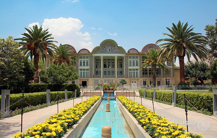 تصویری از باغ ارم شیراز که حوضی در وسط، دو باغچه‌ی گل‌کاری‌شده با گل‌های زرد و درختان نخل در دو طرف به عمارت مرکزی منتهی می‌شود.